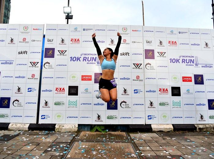 Runner jumping for joy at the Decathlon 10K Run Mumbai finish line, with Abunduntia named on the sponsor wall